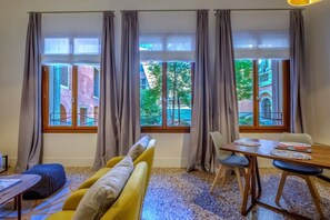 Ein Zimmer mit einer Sitzecke, einem Esstisch und Blick auf ein Gebäude durch große Fenster.