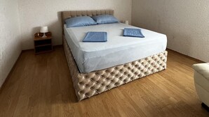 A neatly made bed with a tufted headboard, a bedside table with a lamp, and a wooden floor. - Apartment Lavaran 6 (Vir)