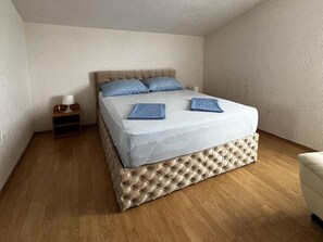 Ein ordentlich bezogenes Bett mit einer gebügelten Kopfteil, ein Nachttisch mit Lampe und Holzboden.