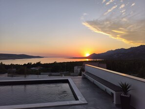 A rooftop pool with a view of a sunset over a body of water and mountains. - Villa Green Horizon With sea View (Jasenice)
