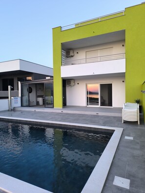A modern building with a swimming pool, a covered outdoor area, and a second floor balcony. - Villa Green Horizon With sea View (Jasenice)