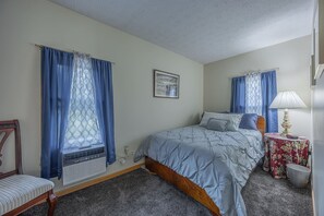 Une chambre à coucher avec un lit, une chaise, une table avec une lampe et une fenêtre avec des rideaux.