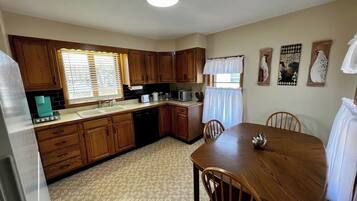 A compact kitchen with wooden cabinets, a dining table, and a refrigerator.