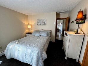 A bedroom with a bed, bedside lamp, dresser, and a hallway leading to a bathroom. - Sun-Filled Upper Gem | Near LECOM & Elmira College (Elmira)