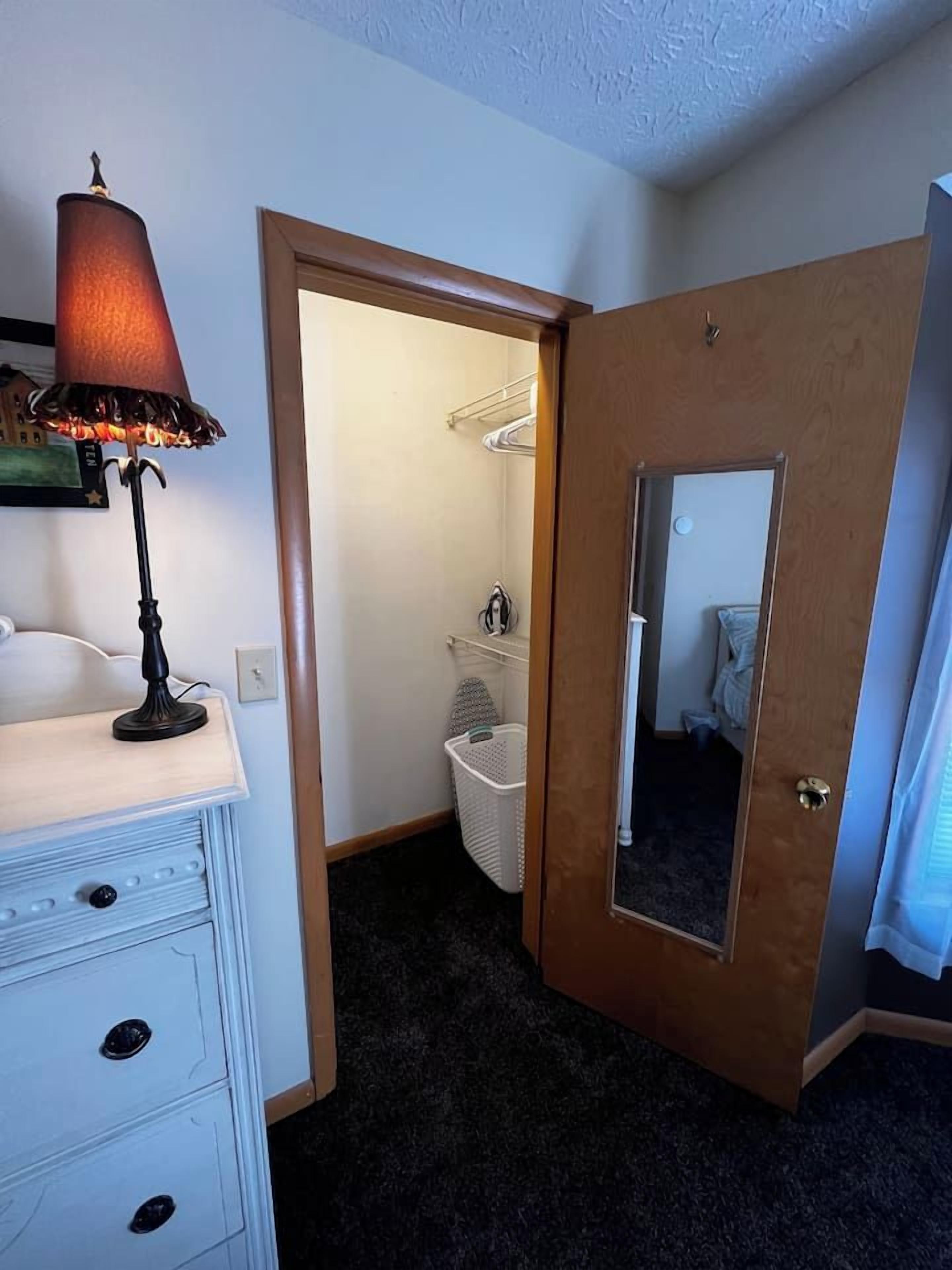 A room with a desk, a lamp, a door leading to a bathroom, and a mirror.