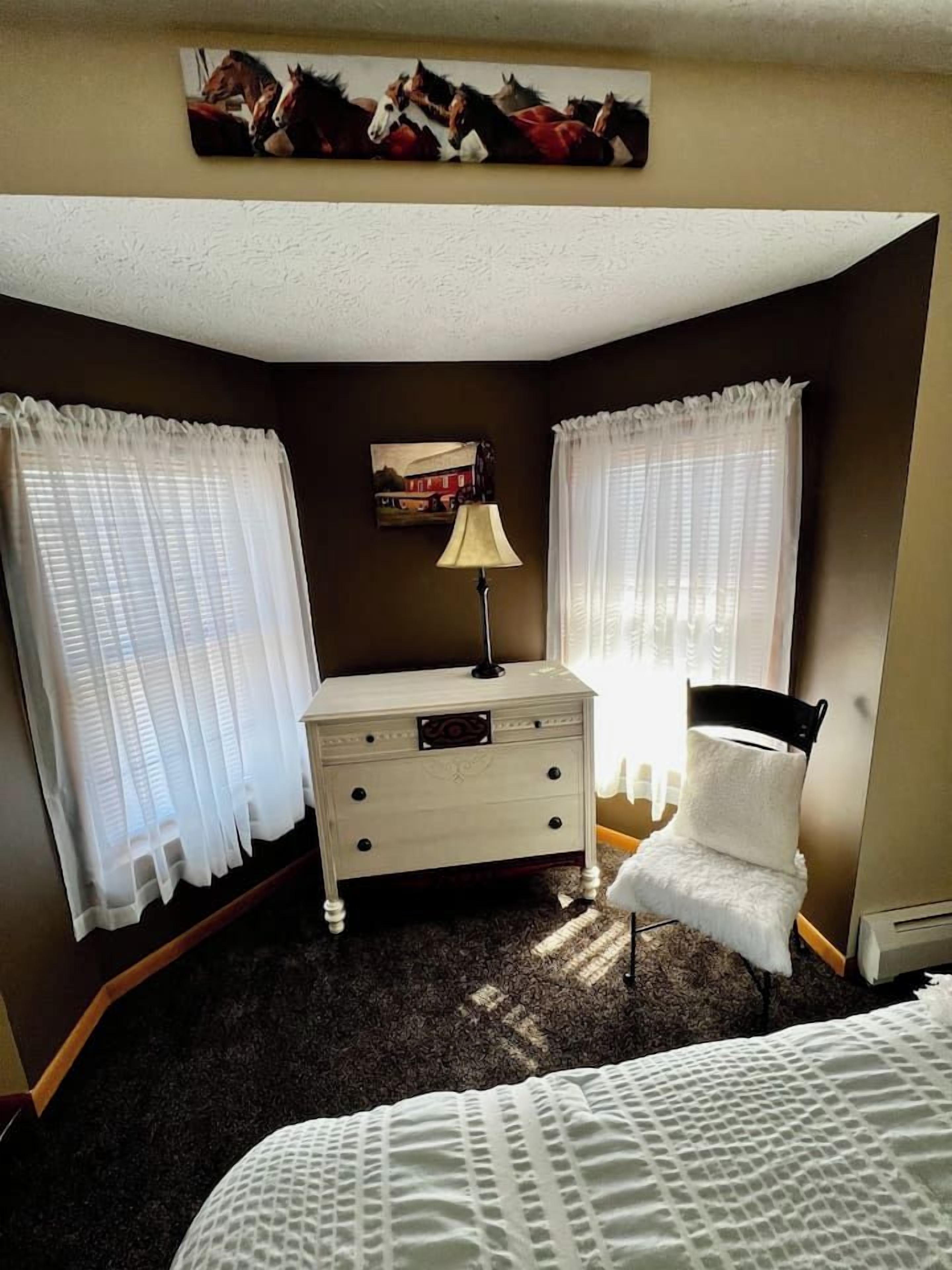 A bedroom with a bed, a chair, a dresser, and curtains.