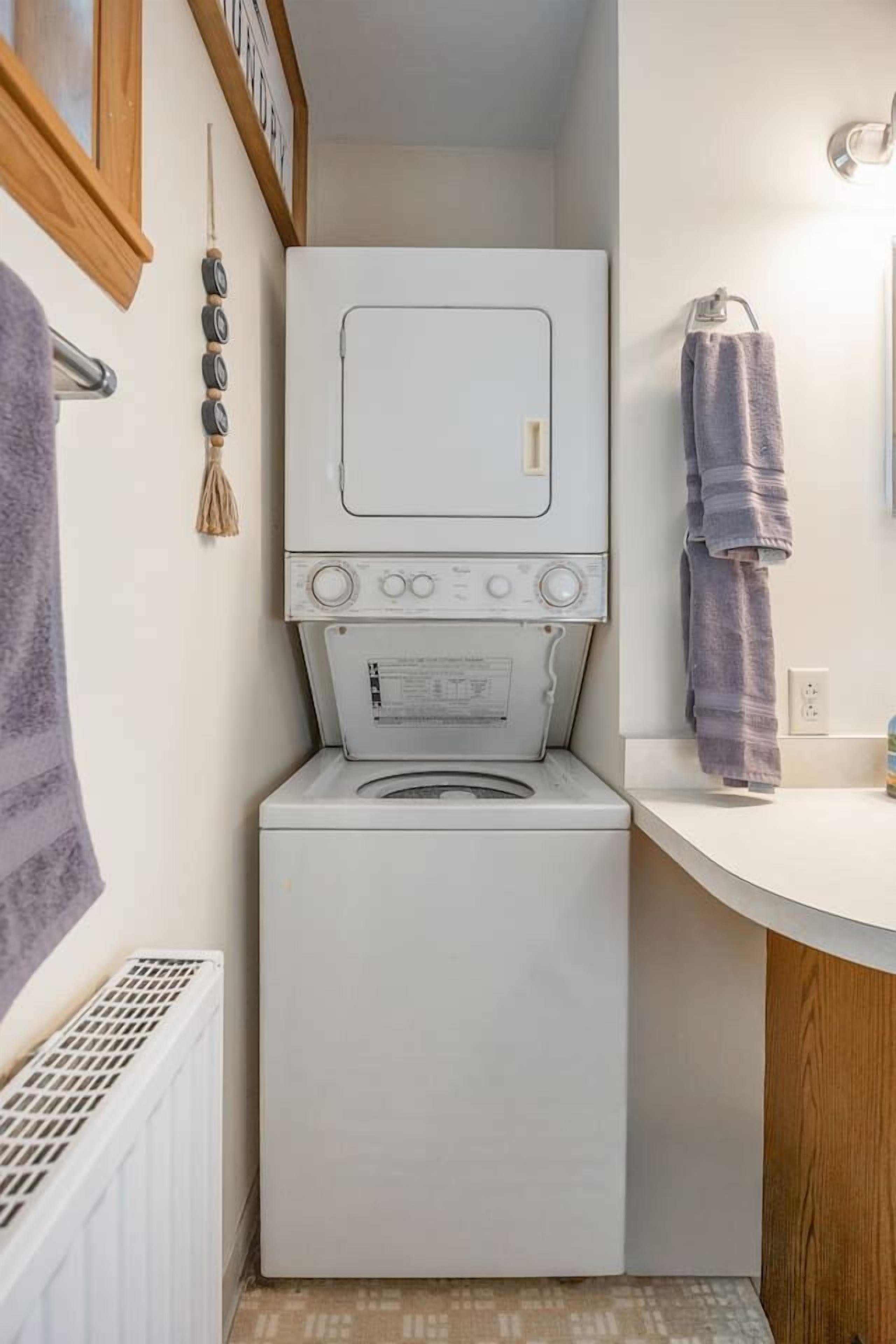 A compact laundry area with a stacked washer and dryer, a white countertop, and a towel rack.