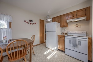 A compact kitchen with wooden cabinets, a white refrigerator, and a stove. - Sun-Filled Upper Gem | Near LECOM & Elmira College (Elmira)