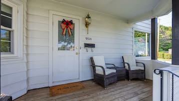 A porch with a white door, two wicker chairs, a mailbox, and a doormat.