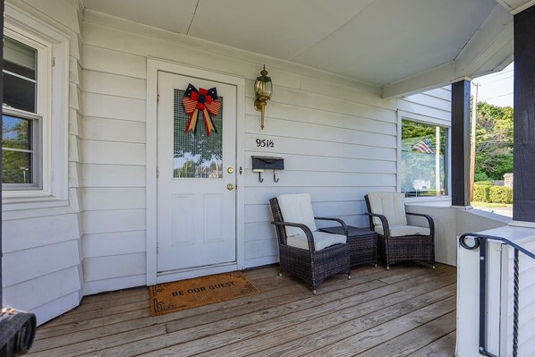 A porch with a white door, two wicker chairs, a mailbox, and a doormat.