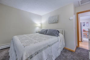 A bedroom with a bed, a nightstand, a lamp, and a door leading to another room. - Sun-Filled Upper Gem | Near LECOM & Elmira College (Elmira)