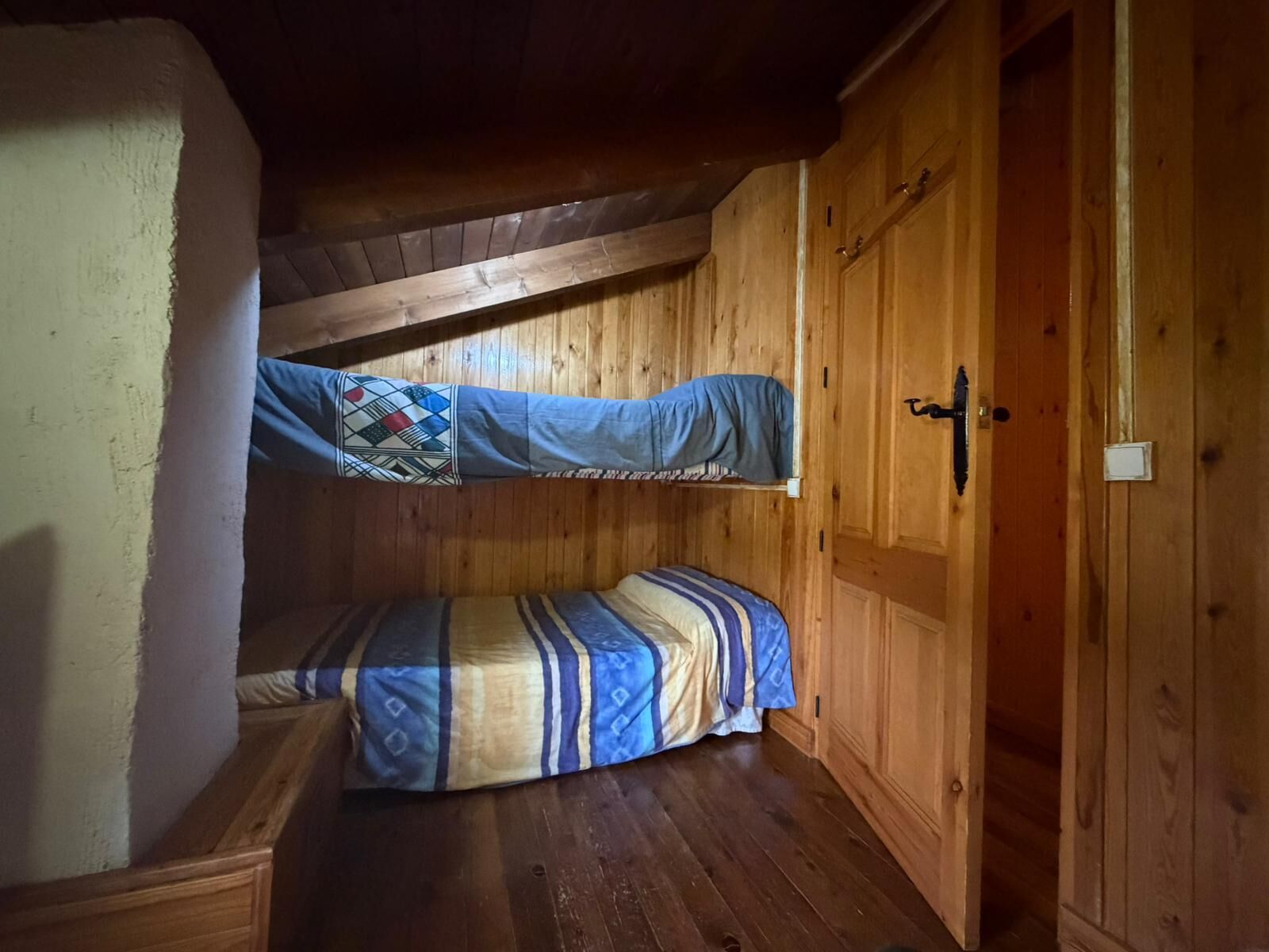 Ein kleiner Raum mit Holzboden, einem Etagenbett und einer Tür.