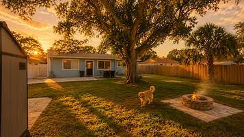 A residential backyard with a house, a tree, a dog, and a fire pit.