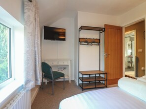 A bedroom with a bed, a desk with a chair, a TV, a coat rack, and a door leading to a bathroom. - Rockhurst Farm (Matlock)