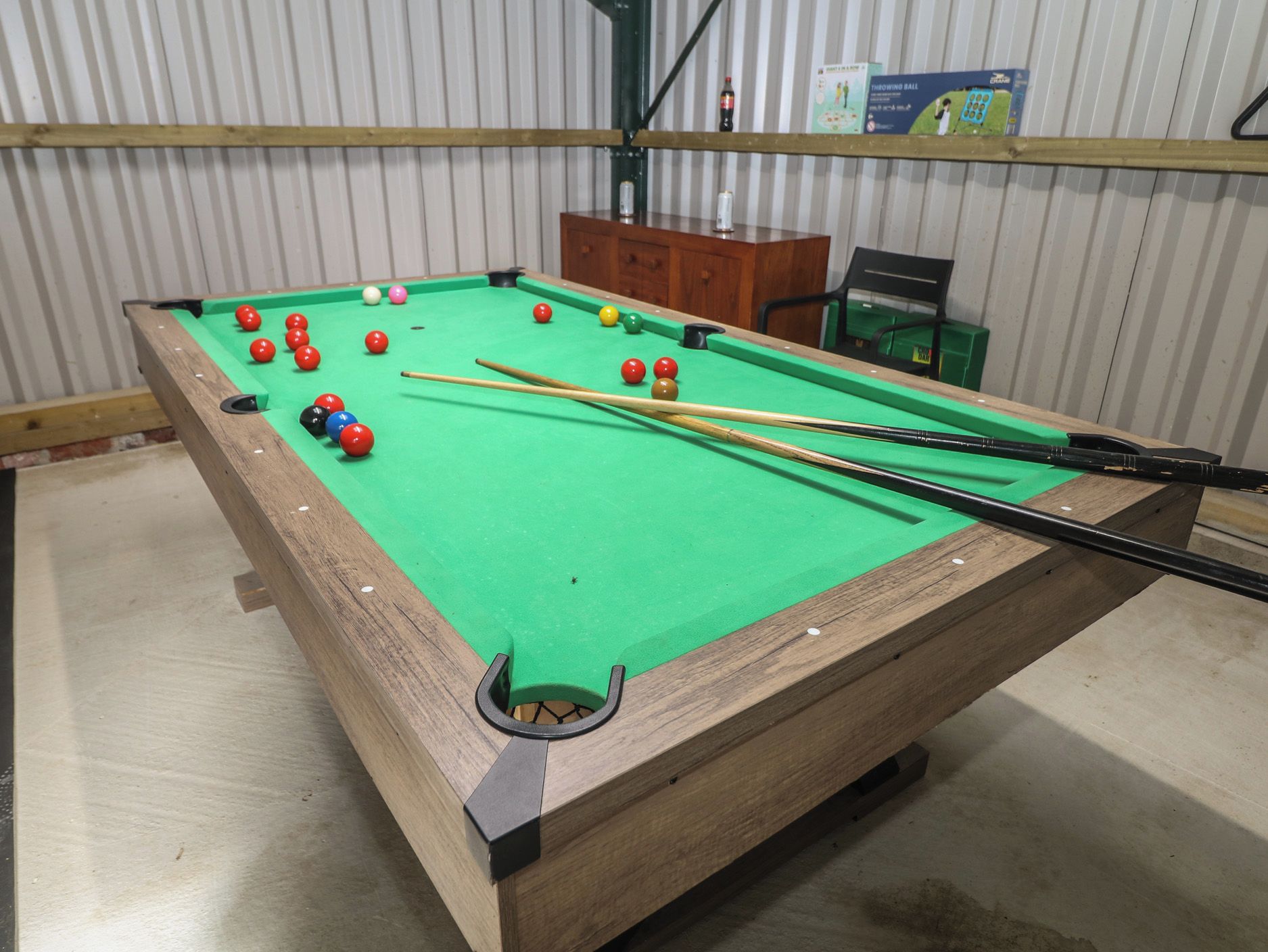 A pool table with balls and cues, a wooden cabinet, and a shelf with books.