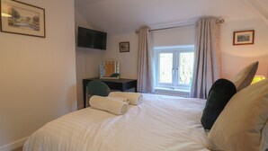 A bedroom with a bed, a desk, a chair, a television, and a window with curtains. - Rockhurst Farm (Matlock)