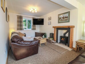 A living room with a leather sofa, a fireplace, a television, and a window with curtains. - Rockhurst Farm (Matlock)
