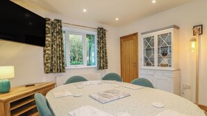 A dining area with a round table, chairs, a wooden sideboard, a window with curtains, and a cabinet with glass doors. - Rockhurst Farm (Matlock)