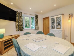 A dining area with a round table, chairs, a wooden sideboard, a window with curtains, and a cabinet with glass doors. - Rockhurst Farm (Matlock)