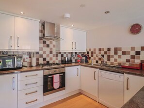 A modern kitchen with white cabinets, a microwave, a stove, a dishwasher, and a checkered backsplash. - Beck House (Weymouth)