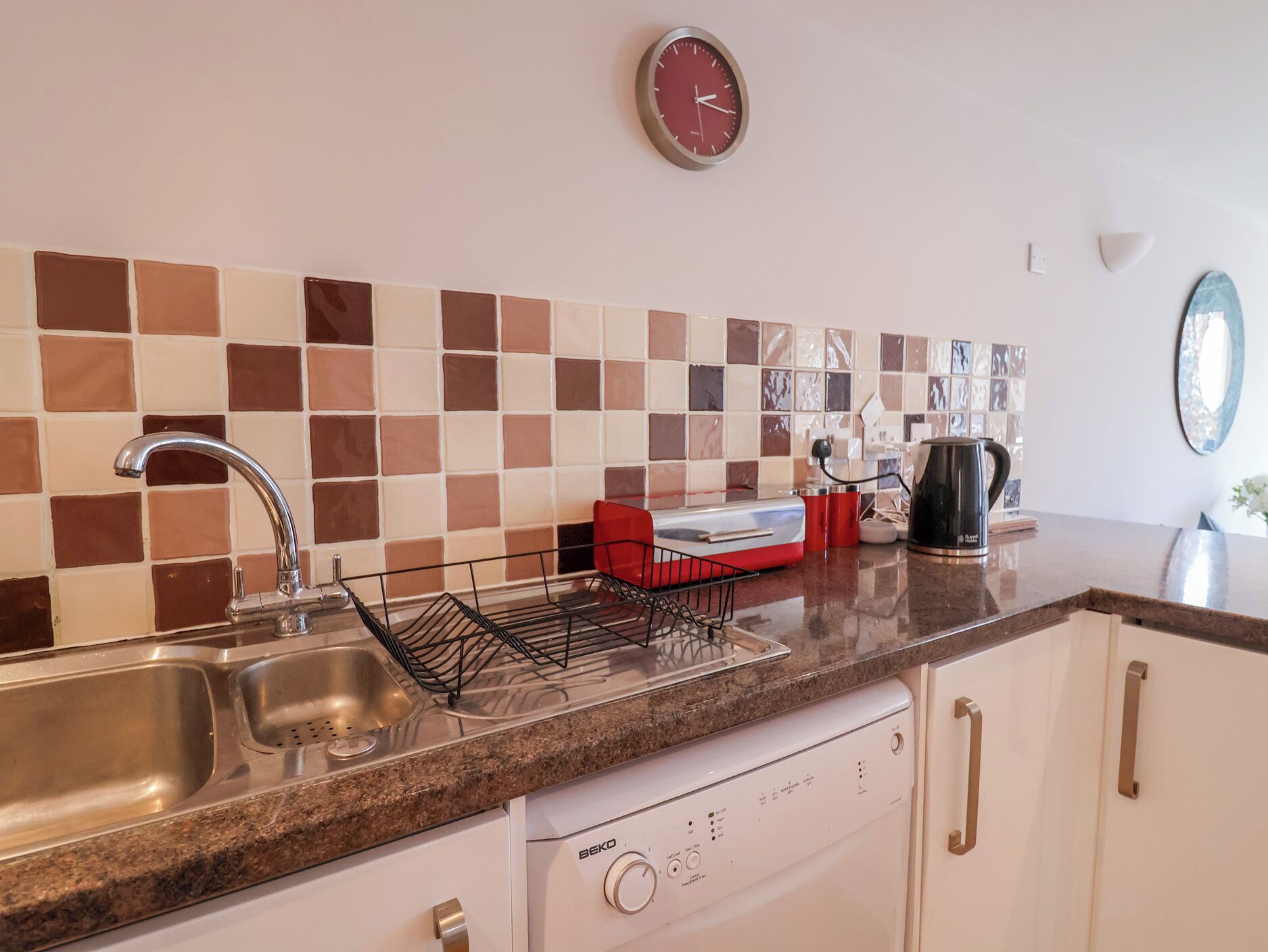 Una cocina con un lavamanos, un escurreplatos, una cafetera y un reloj en la pared.