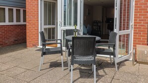 En åben patio med et bord, stole, en vinflaske og en murstensvæg.