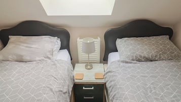 Quarto duplo com duas camas, uma mesa de cabeceira, uma luminária e um radiador.