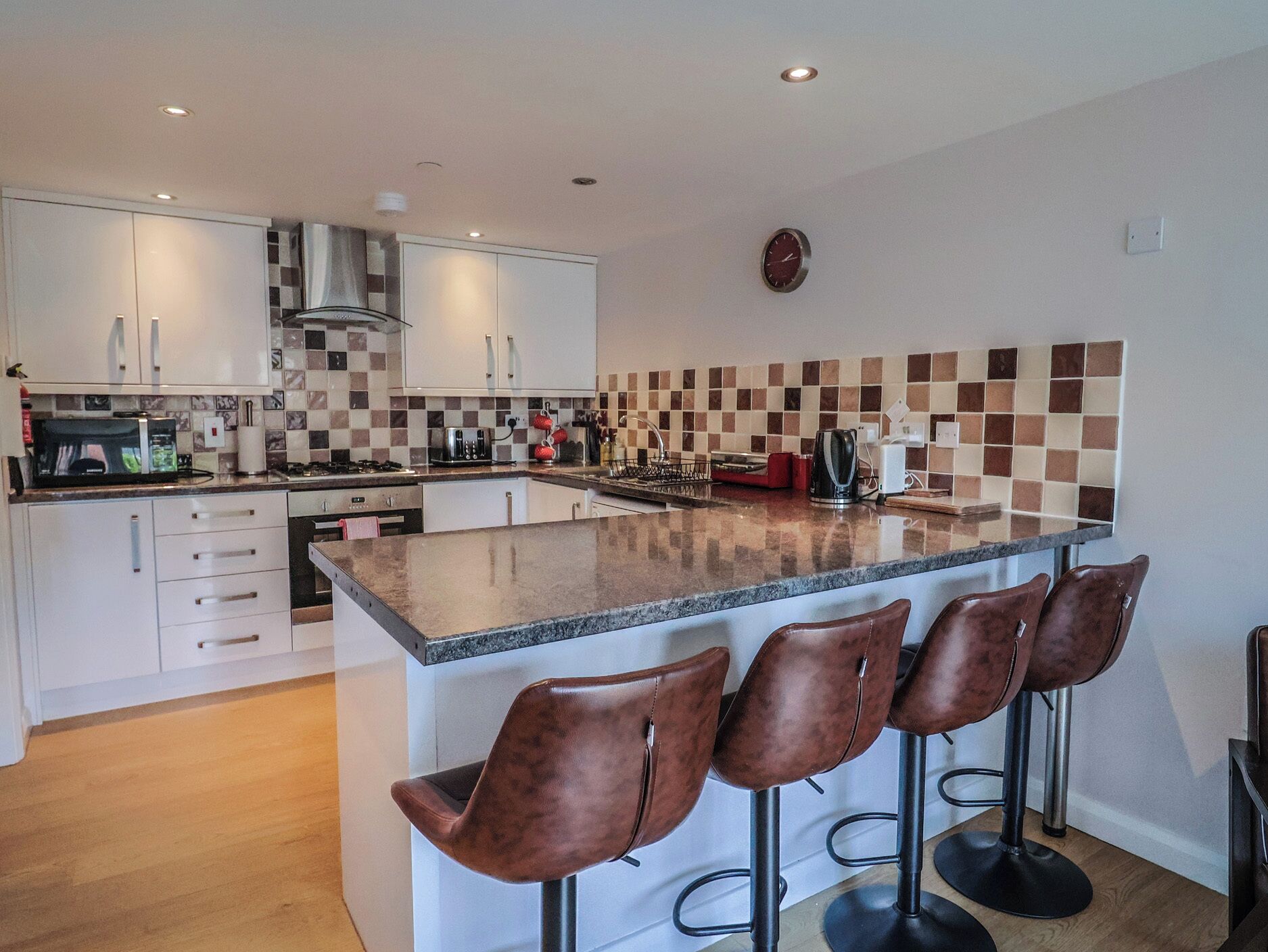A modern kitchen with white cabinets, a central island with bar stools, a microwave, and a clock on the wall.