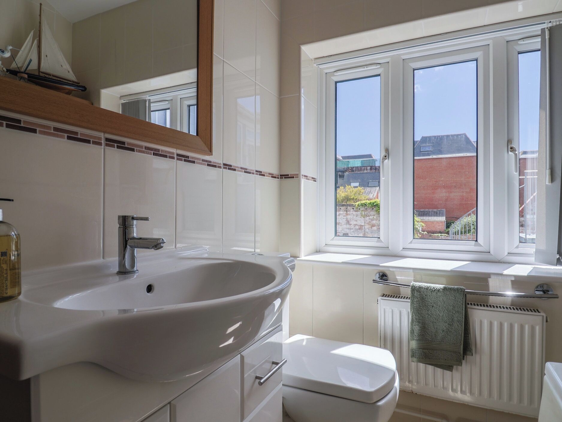 A bathroom with a white sink, a toilet, a window with a view of buildings, and a radiator.