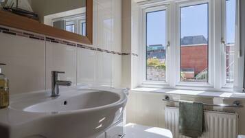 A bathroom with a white sink, a toilet, a window with a view of buildings, and a radiator.
