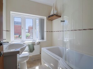 A bathroom with a bathtub, toilet, sink, and a window with a view of buildings outside. - Beck House (Weymouth)