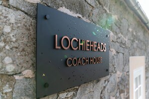 Une plaque portant l’inscription « LOCHIEHEADS COACH HOUSE » est fixée à un mur de pierre.