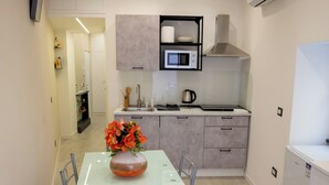 Een moderne keuken met een eethoek, met een glazen tafel, metalen stoelen, een magnetron en een inbouwoven.