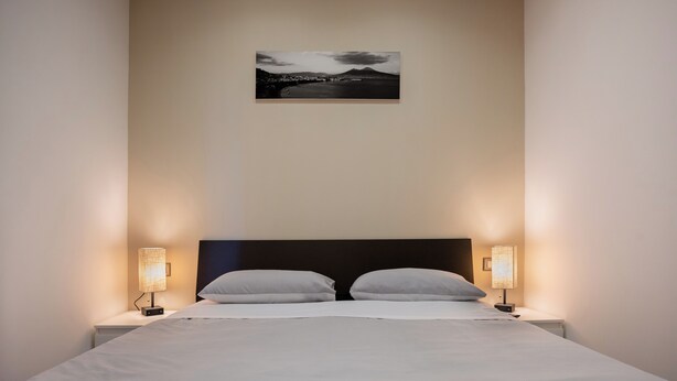 Een net opgemaakt bed met twee kussens, een hoofdbord en twee bedlampjes.