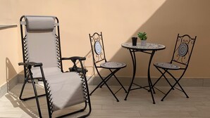 Een balkon met een opklapbare stoel, twee kleine tafels en plantenpotten.