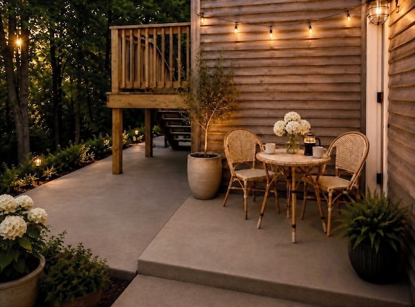 Une terrasse extérieure avec une plateforme en bois, des chaises en osier, une table ronde et des plantes en pot.