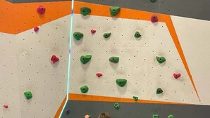 Un niño trepando una pared con agarraderas de colores, rodeado de bloques de espuma azul.