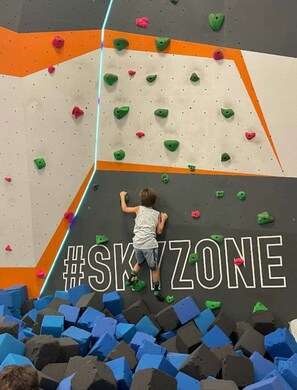 Ein Kind klettert an einer Wand mit bunten Griffen, umgeben von blauen Schaumstoffbausteinen.