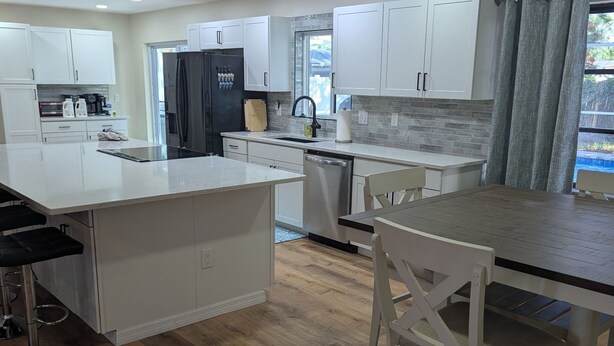 Una cocina moderna con armarios blancos, una isla central y un comedor con una mesa y sillas.