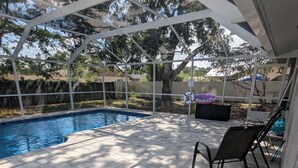Un espacio exterior techado con piscina, suelo de baldosas y una silla.
