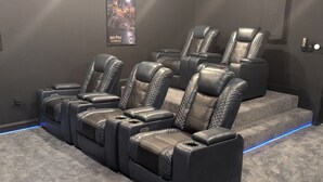 Un cine en casa con sillones de cuero reclinables, un proyector y un cartel en la pared.
