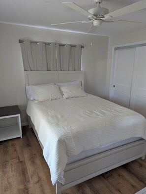 Ein Schlafzimmer mit einem Bett, einem Nachttisch, einem Deckenventilator und einer Tür.
