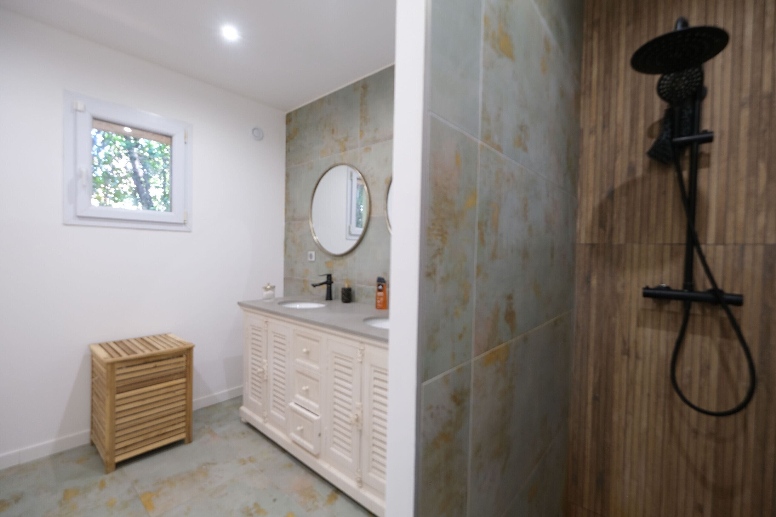 A bathroom with a wooden shower enclosure, a sink with a mirror, and a small wooden stool.