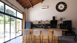 Una cocina moderna con una isla de madera, taburetes de bar, un reloj grande y vistas al exterior.