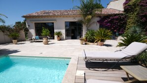 Un área de piscina con sillones de descanso, un patio y un edificio con techo de tejas.