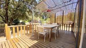 An outdoor wooden deck with a table and chairs, surrounded by a wooden fence and trees.