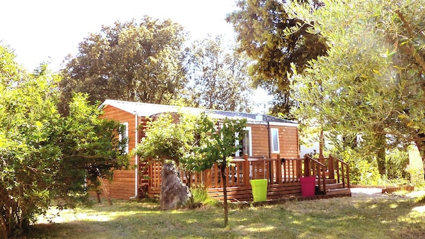 A wooden cabin with a deck, surrounded by trees and grass.