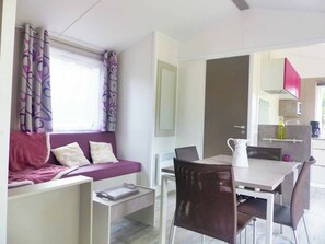 A modern room with a purple sofa, a dining table with chairs, a kitchen area with cabinets and a sink, and a window with curtains.