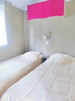 A room with two beds, a window, a wall-mounted light, and a pink cabinet.