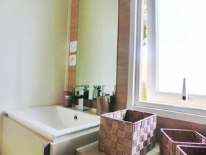 A bathroom with a bathtub, a mirror, a window, and wicker baskets.
